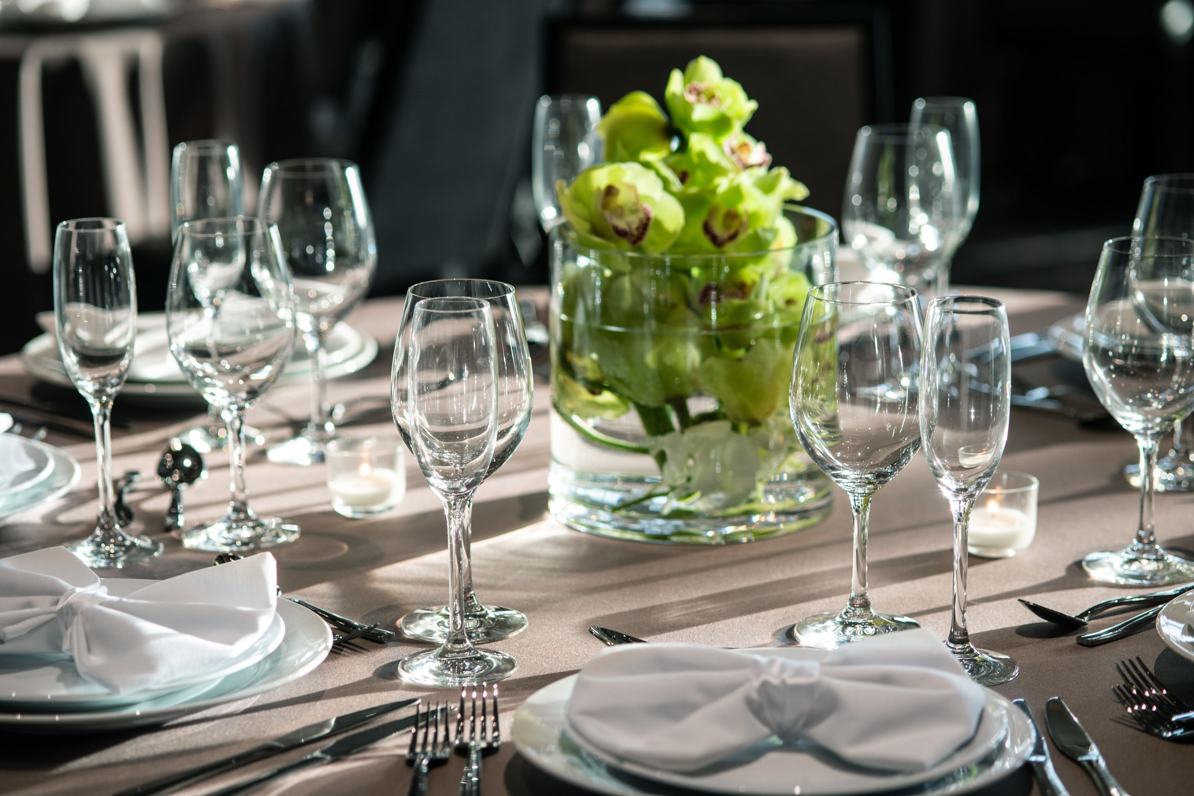 A dining table set with multiple wine glasses, plates, and cutlery, with a centerpiece of green flowers.