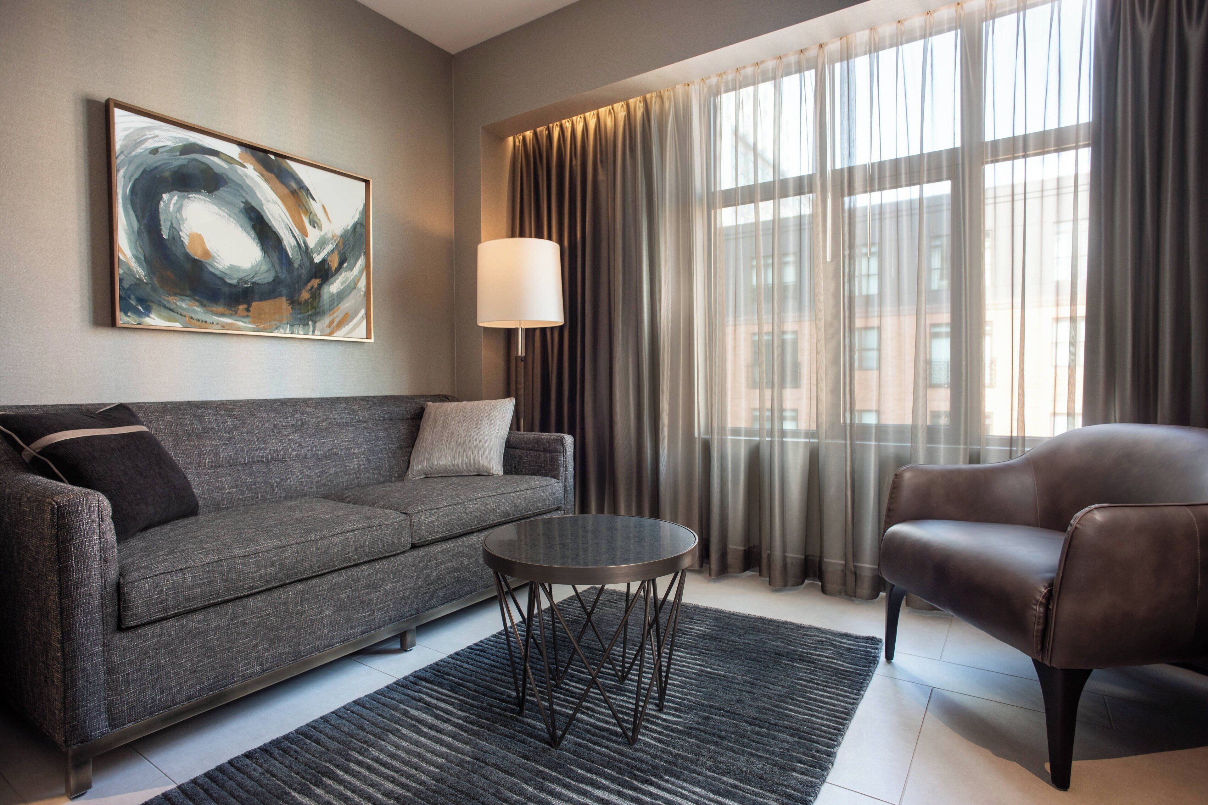 A modern living room with a grey sofa, a leather armchair, a round coffee table, and a large abstract painting on the wall.