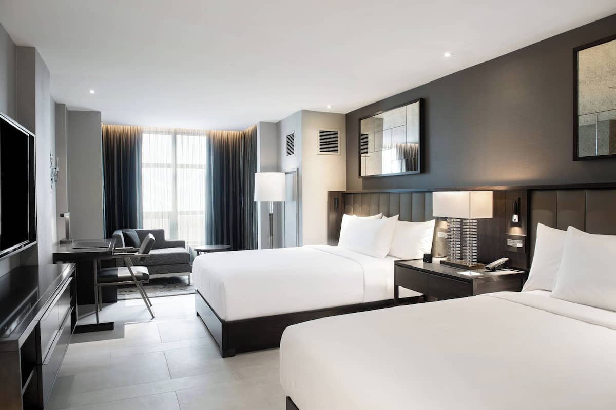 Ein modernes Hotelzimmer mit zwei Betten, einem Schreibtisch, einem Fernseher und einem großen Fenster mit Vorhängen.