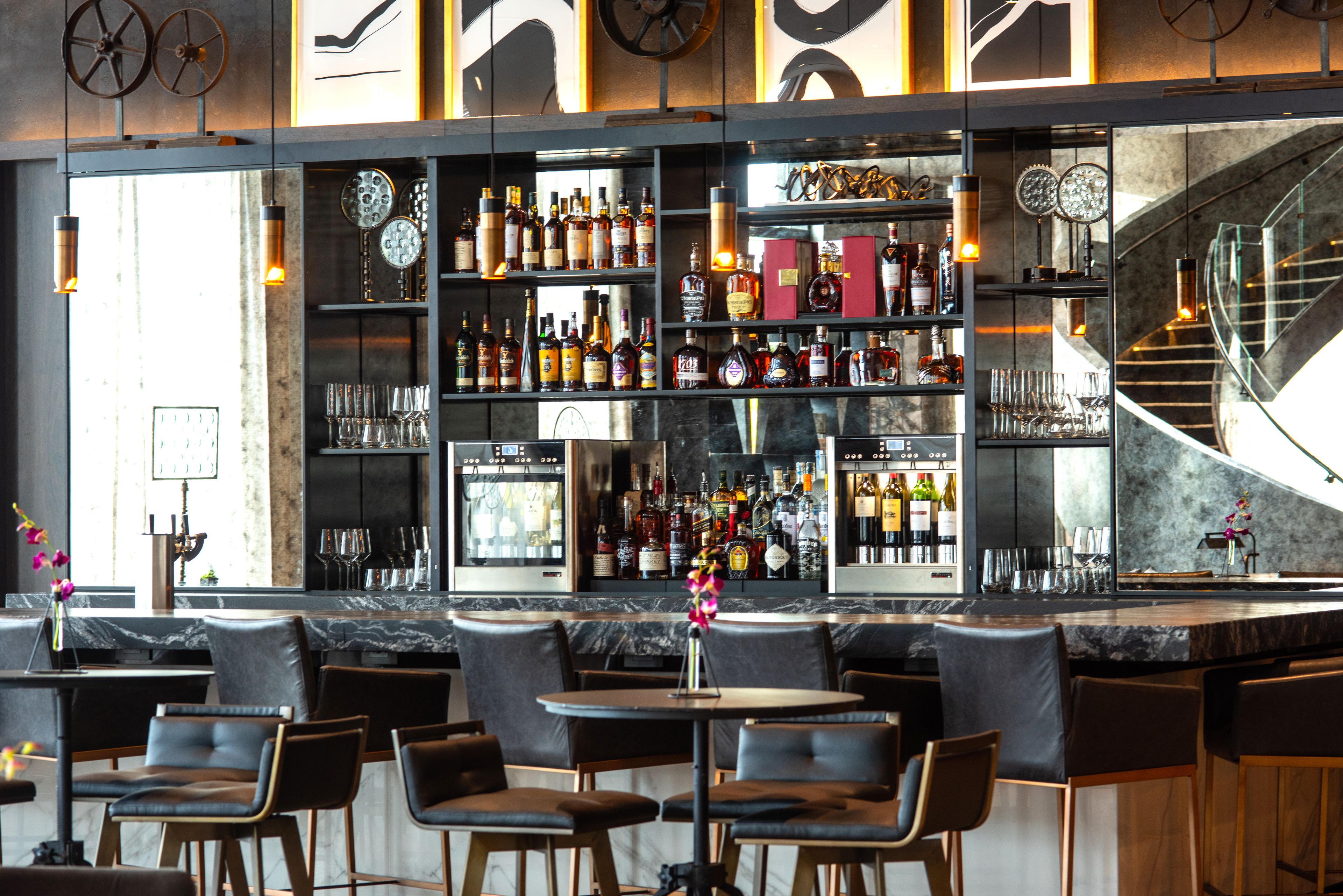 A bar area with seating, shelves of bottles, and a staircase.