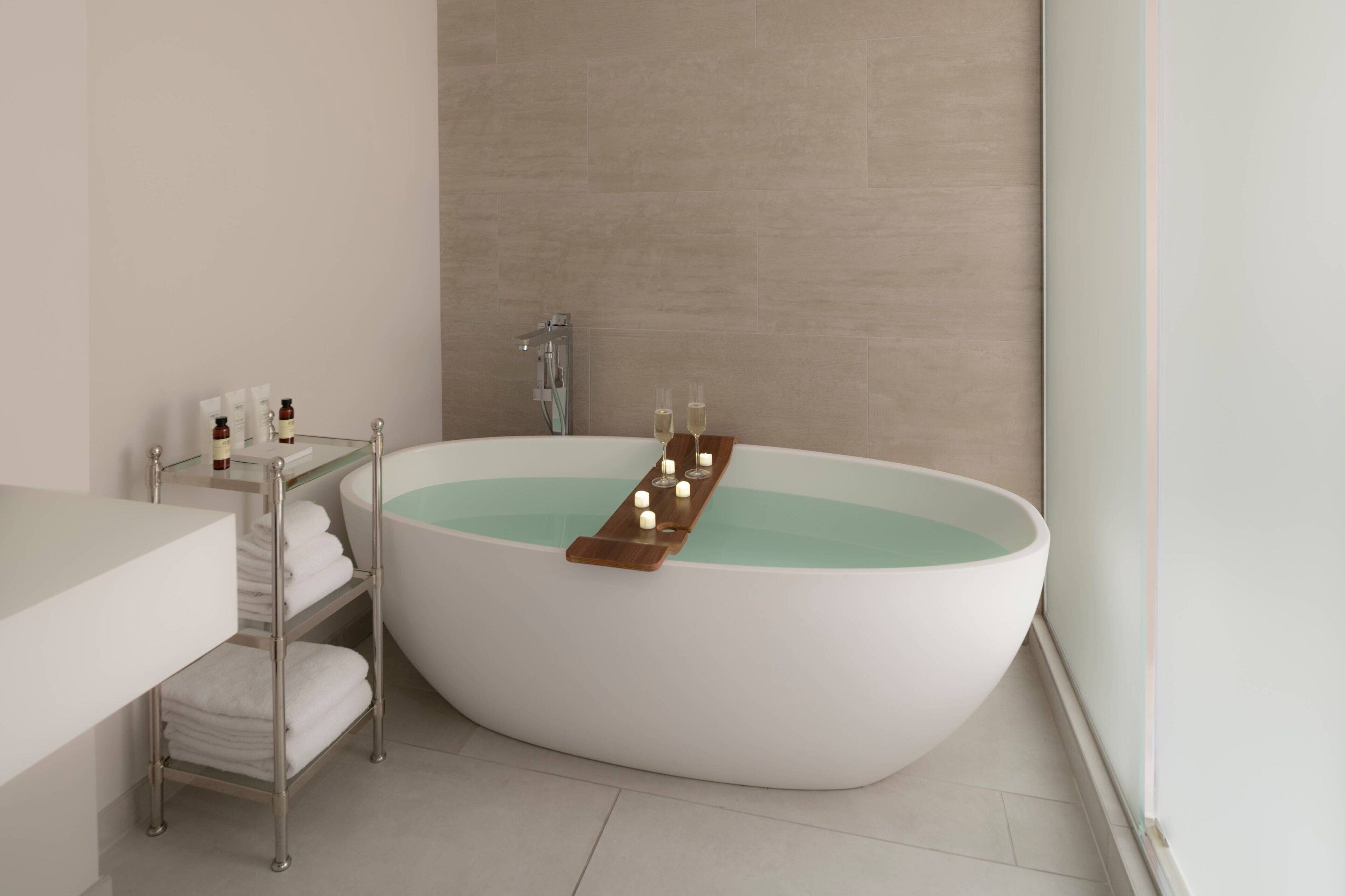 A modern bathroom with a freestanding bathtub, a glass shelf with toiletries, and a towel rack.