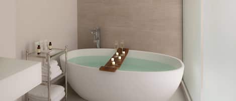 Ein modernes Badezimmer mit freistehender Badewanne, einer Glasablage für Pflegeprodukte und einem Handtuchhalter.
