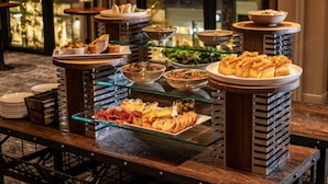 A buffet setup with various food items on glass shelves and plates, arranged on a wooden table. - The Row Hotel at Assembly Row, Autograph Collection (Somerville)