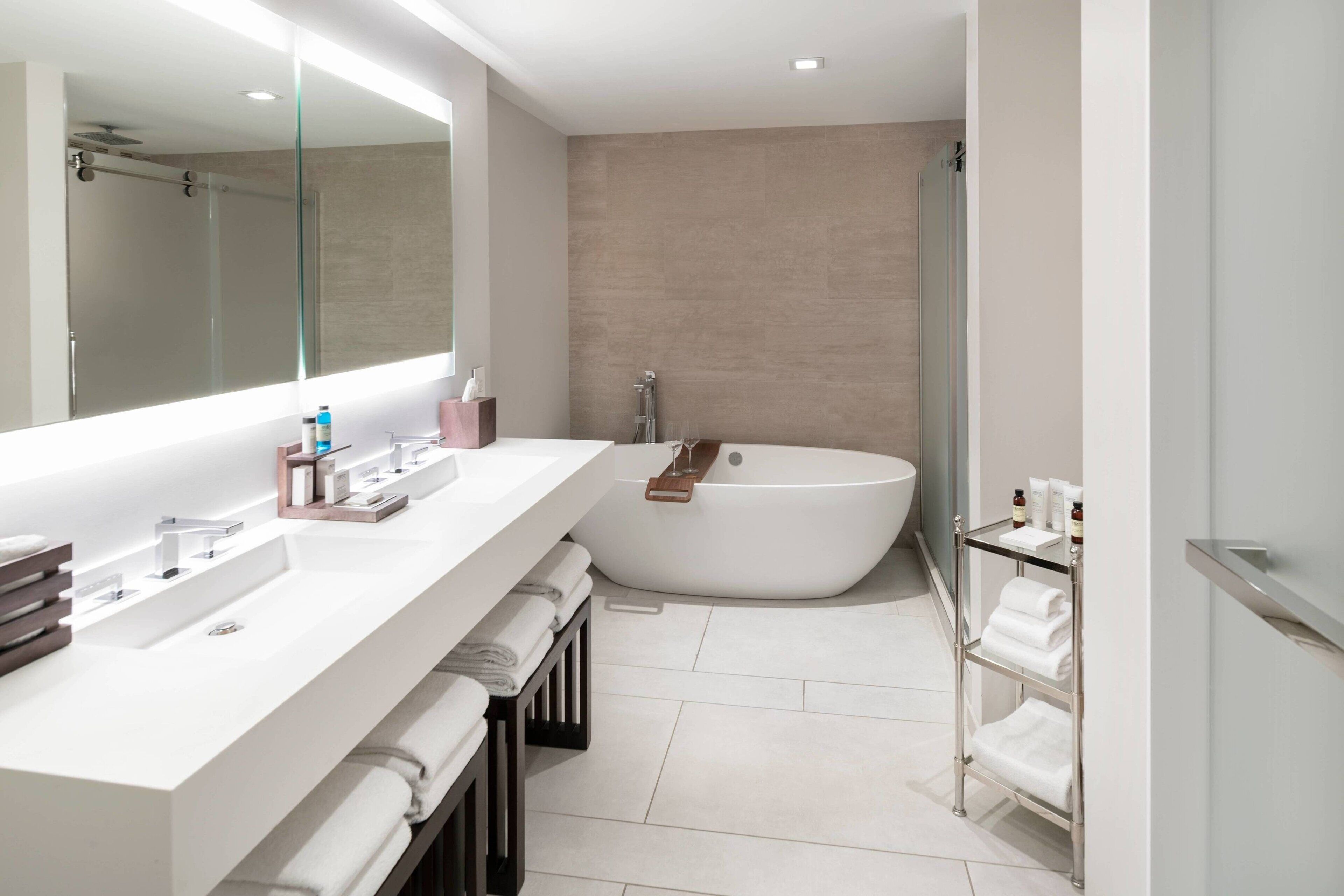 Ein modernes Badezimmer mit einem großen Spiegel, einer weißen Badewanne und einem Waschtisch mit Spüle und Handtuchhalter.