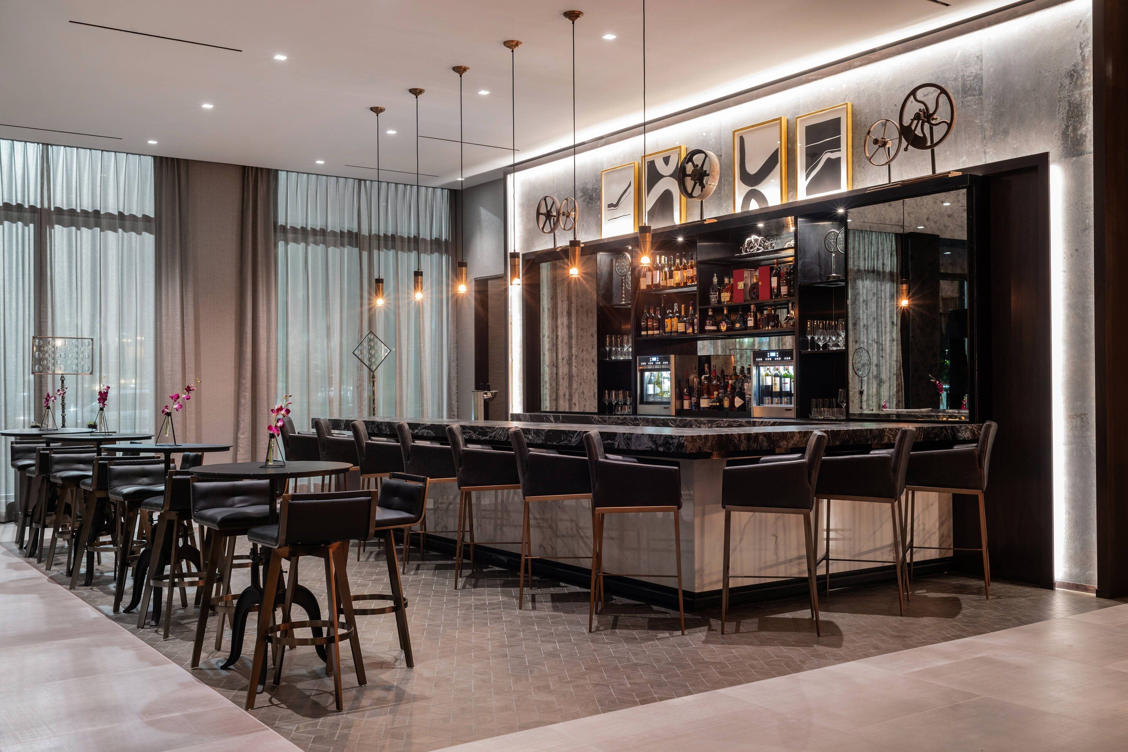 A modern bar area with a marble countertop, black bar stools, and a selection of bottles and glasses.