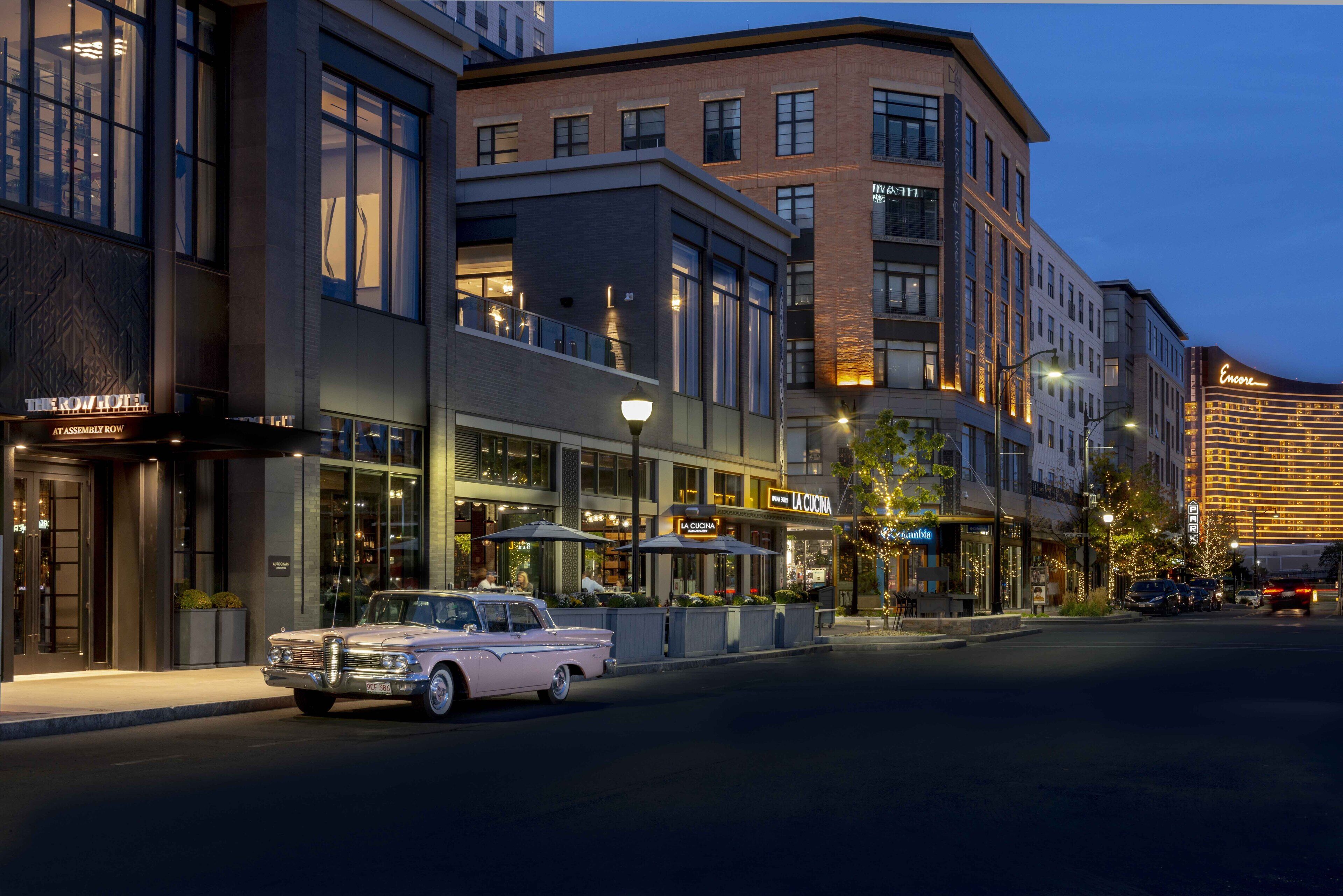 A classic car parked in front of a modern building with a restaurant and a hotel.