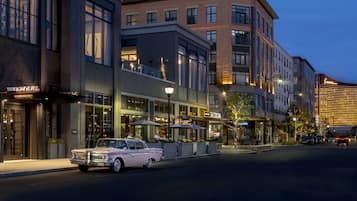 A classic car parked in front of a modern building with a restaurant and a hotel.