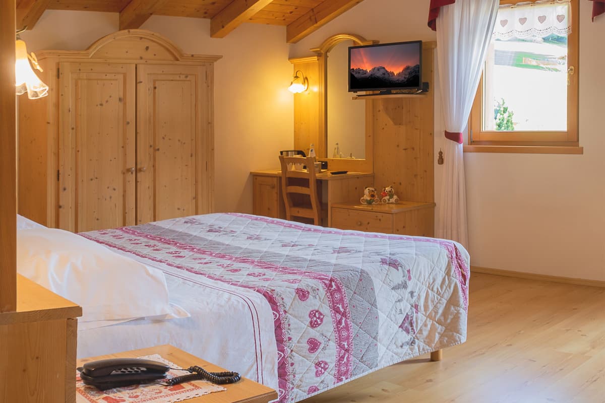 A bedroom with a bed, a desk, a chair, a TV, and a window with curtains.