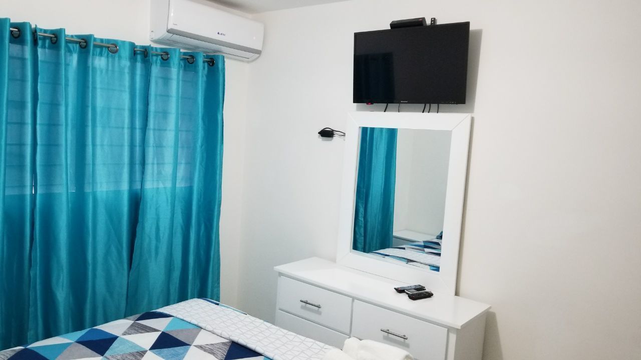 A bedroom with a bed, a white dresser, a mirror, and a TV mounted on the wall.
