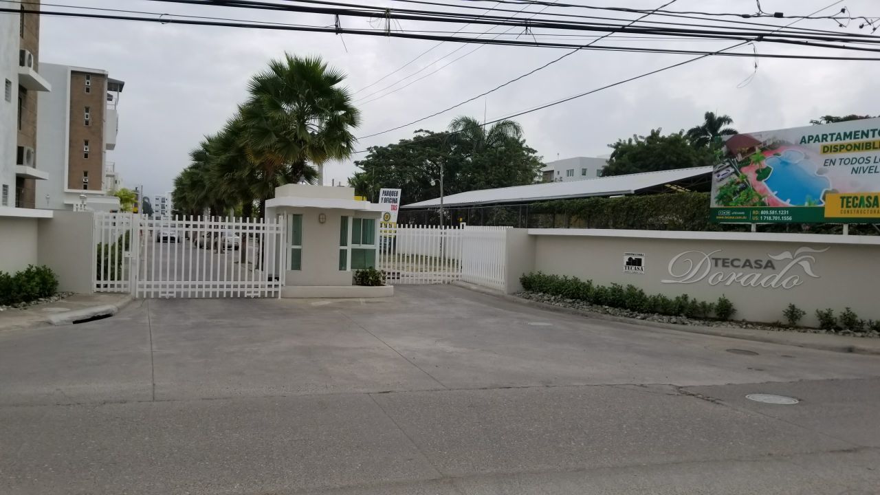A gated entrance to a residential area with a sign for 'APARTMENTO DISPONIBLE EN TODOS LOS NIVELES' and 'TECASA Dorado'.