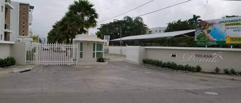 A gated entrance to a residential area with a sign for 'APARTMENTO DISPONIBLE EN TODOS LOS NIVELES' and 'TECASA Dorado'.
