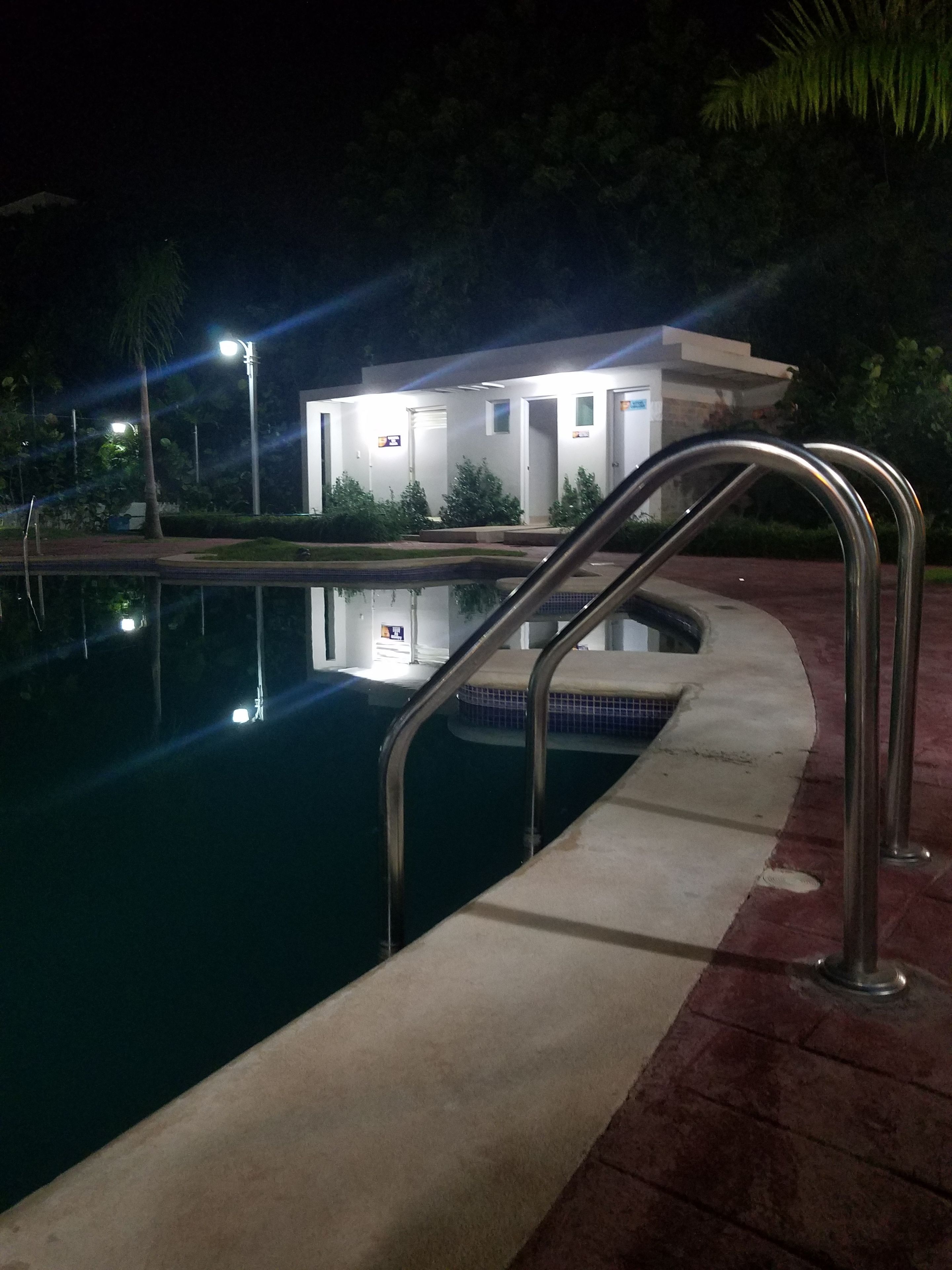 Una piscina con barandillas metálicas, un edificio con varias puertas al fondo y una zona bien iluminada.
