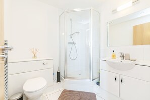 A modern bathroom with a glass-enclosed shower, a white sink, and a toilet. - Premium London Excel Apartment (London)