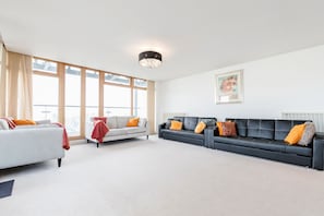 A spacious living room with two sofas, large windows, a chandelier, and a framed artwork on the wall. - Premium London Excel Apartment (London)