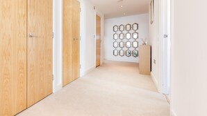 A hallway with wooden doors, a light-colored carpet, and a wall with hexagonal mirrors. - Premium London Excel Apartment (London)