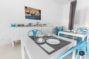 A modern dining area with white furniture, blue chairs, and a painting above the counter. - Hybla Major B&B (Avola)
