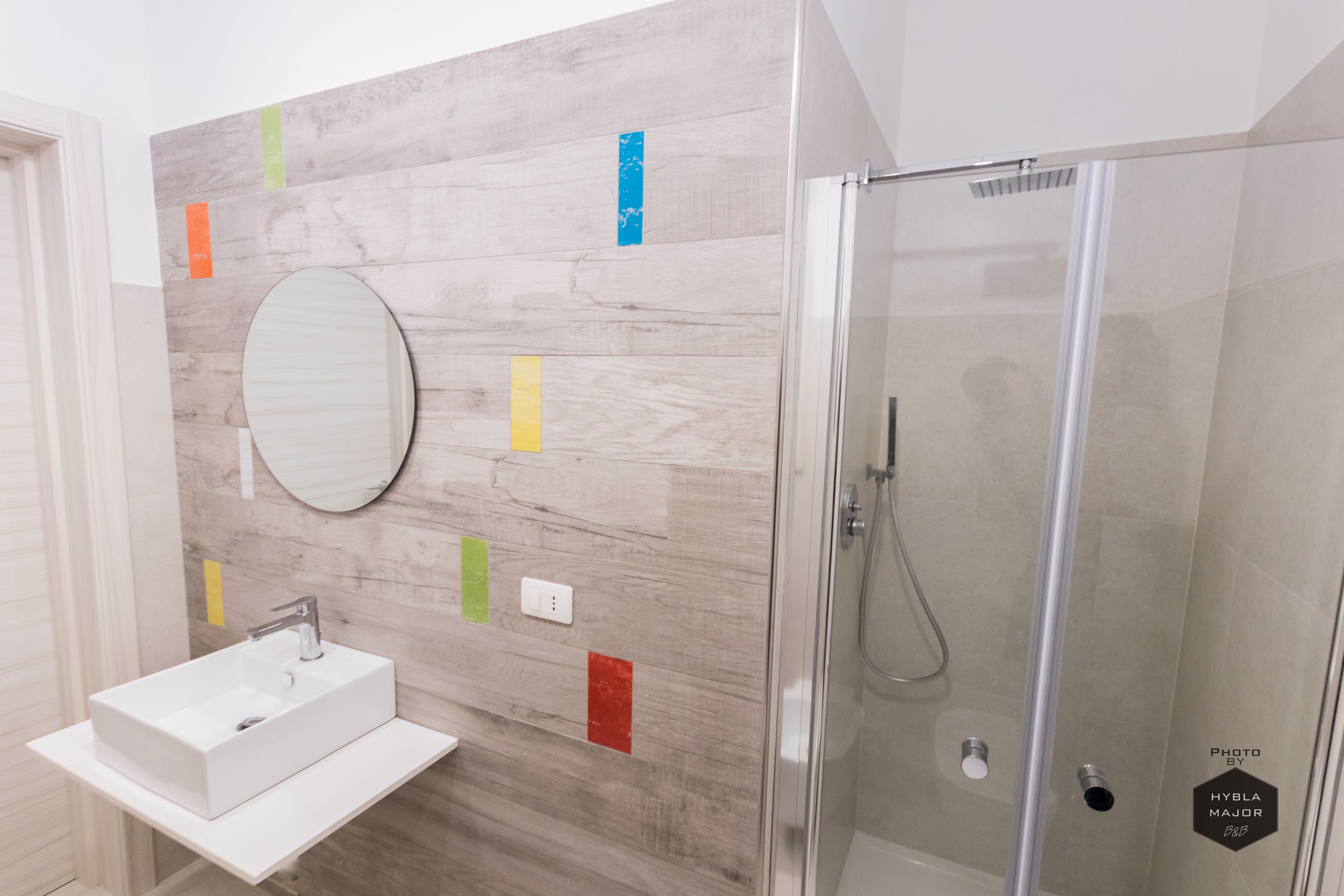 Une salle de bain moderne avec un lavabo blanc, un miroir rond et une douche à parois de verre.