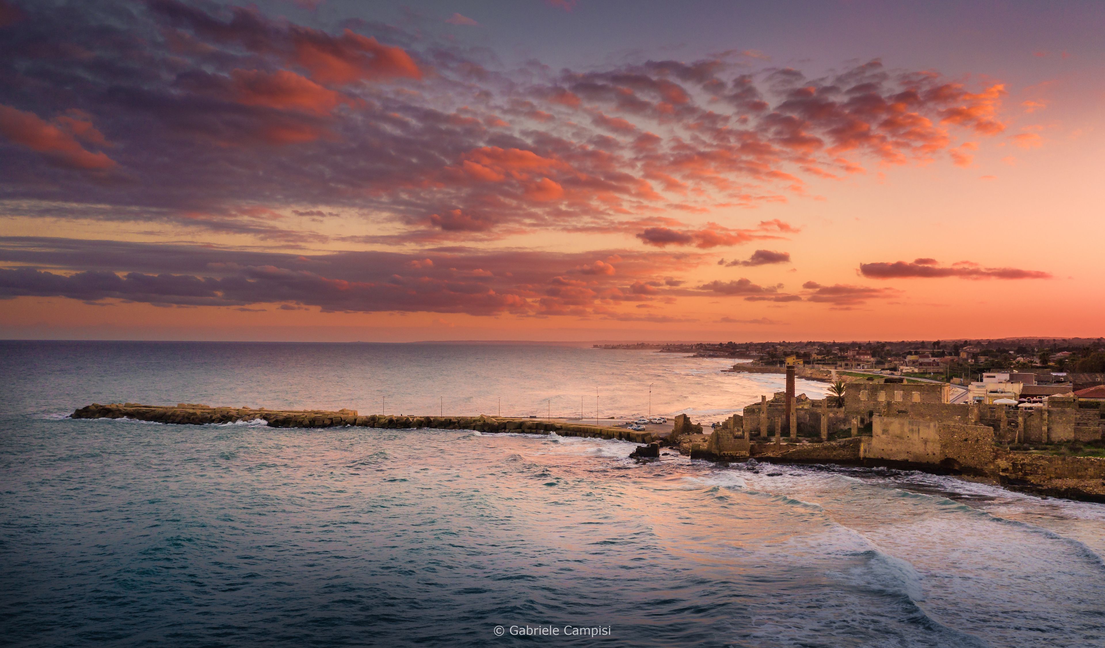 Un paysage urbain côtier avec un ancien mur de pierre et des ruines, dominant la mer.