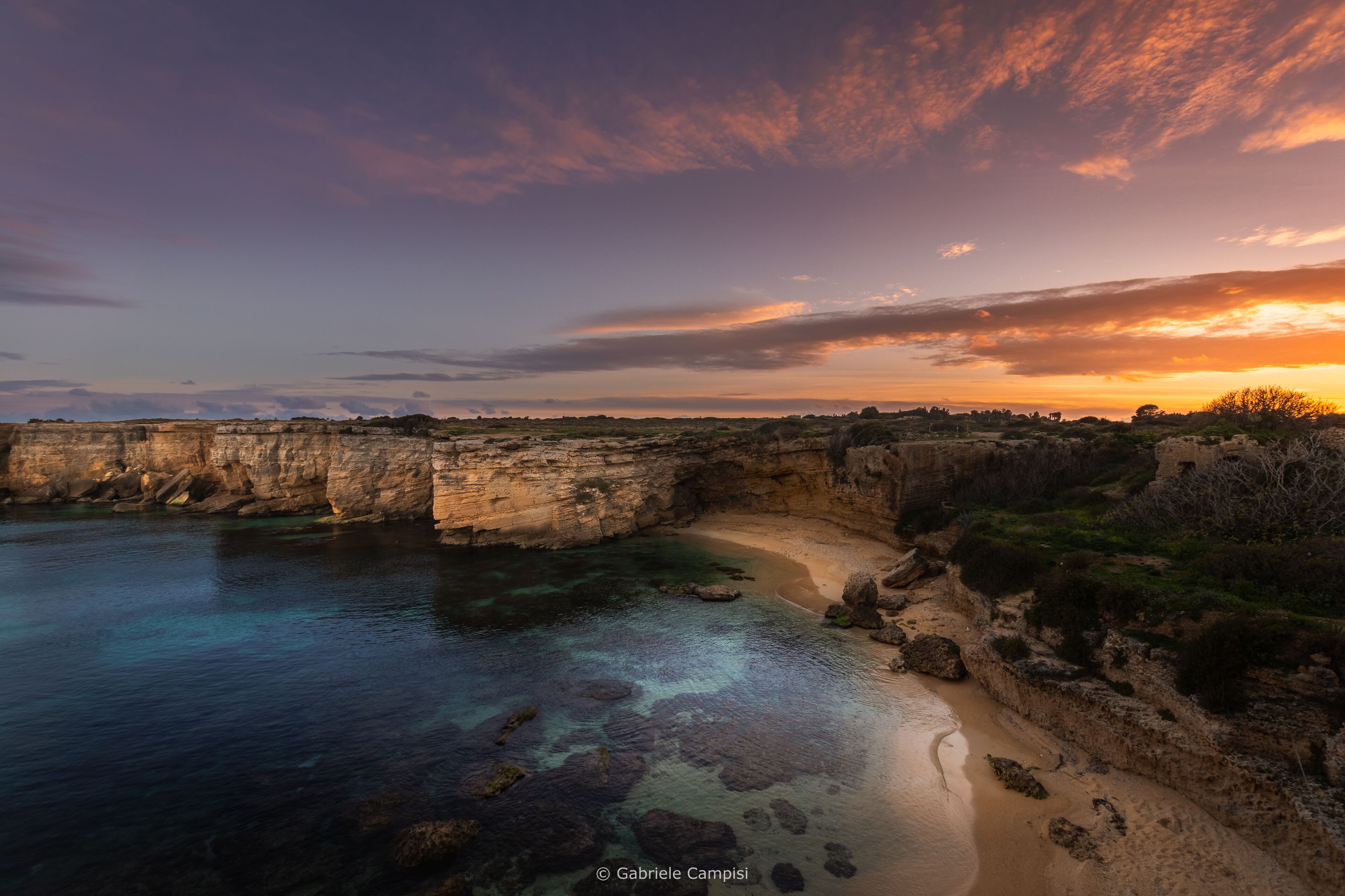 Un paisaje costero con agua cristalina, formaciones rocosas y un atardecer.