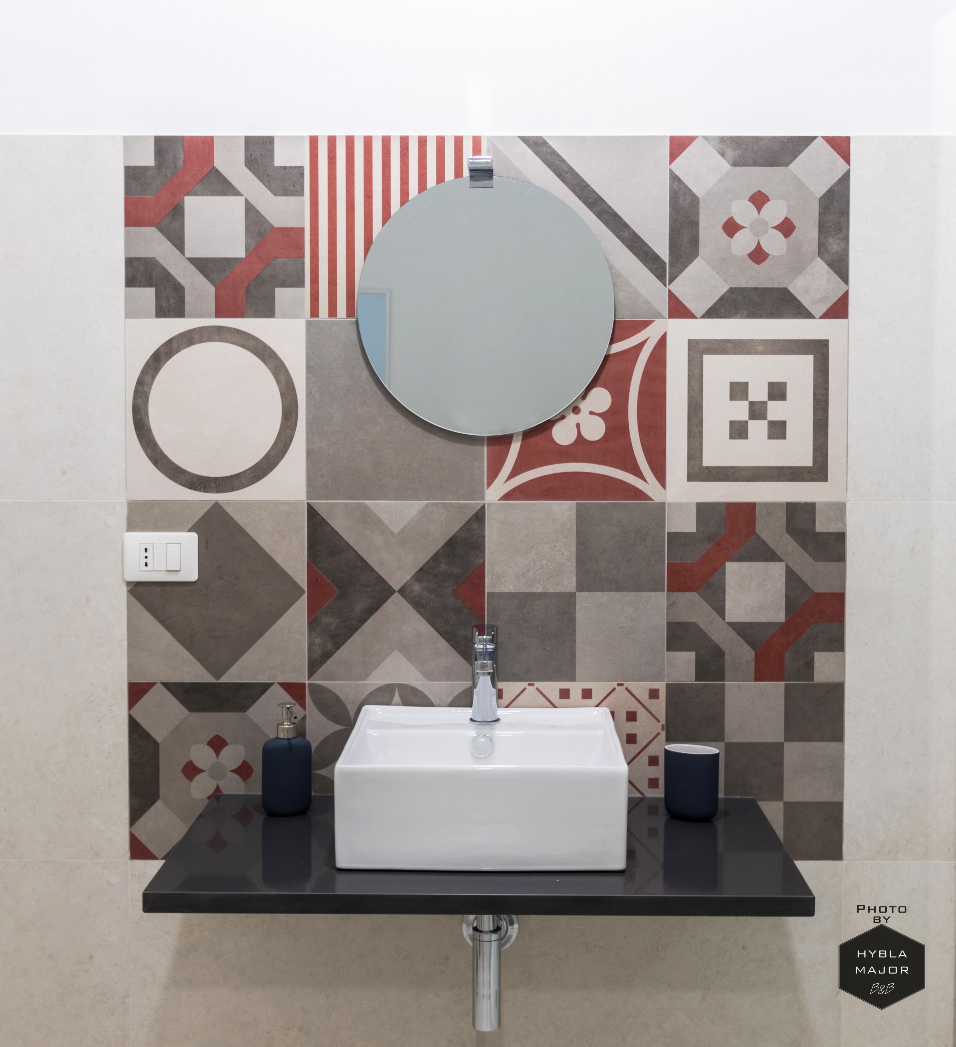 Un bagno con un lavandino bianco, uno specchio rotondo e piastrelle decorate.