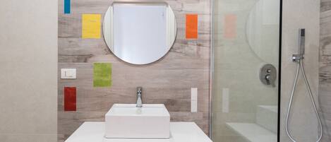 A modern bathroom with a white sink, a round mirror, and a shower.