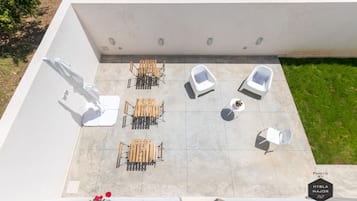 Un patio al aire libre con una mesa y sillas, una silla blanca y una pequeña mesa con una planta.