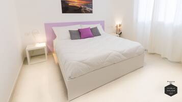Un dormitorio moderno con una cama blanca, un cabecero morado y un cuadro de atardecer sobre la cama.