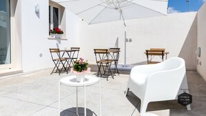Un espacio exterior con mobiliario blanco, que incluye una mesa, sillas y una bañera blanca.