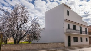 Un edificio moderno con fachada plana, un balcón con barandilla de metal y un árbol con flores en primer plano.