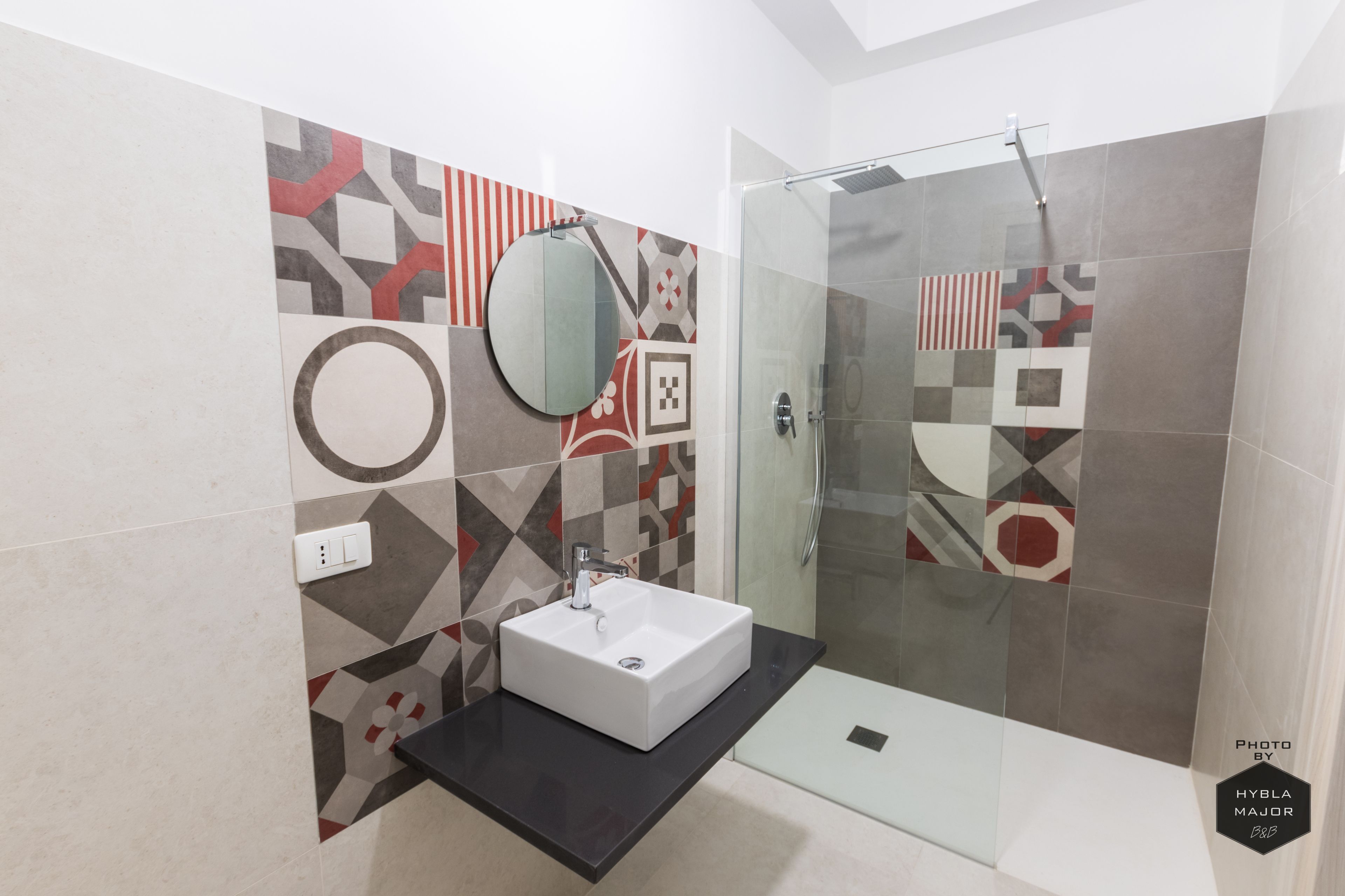 Un baño moderno con un lavamanos rectangular, un espejo redondo y una zona de ducha.
