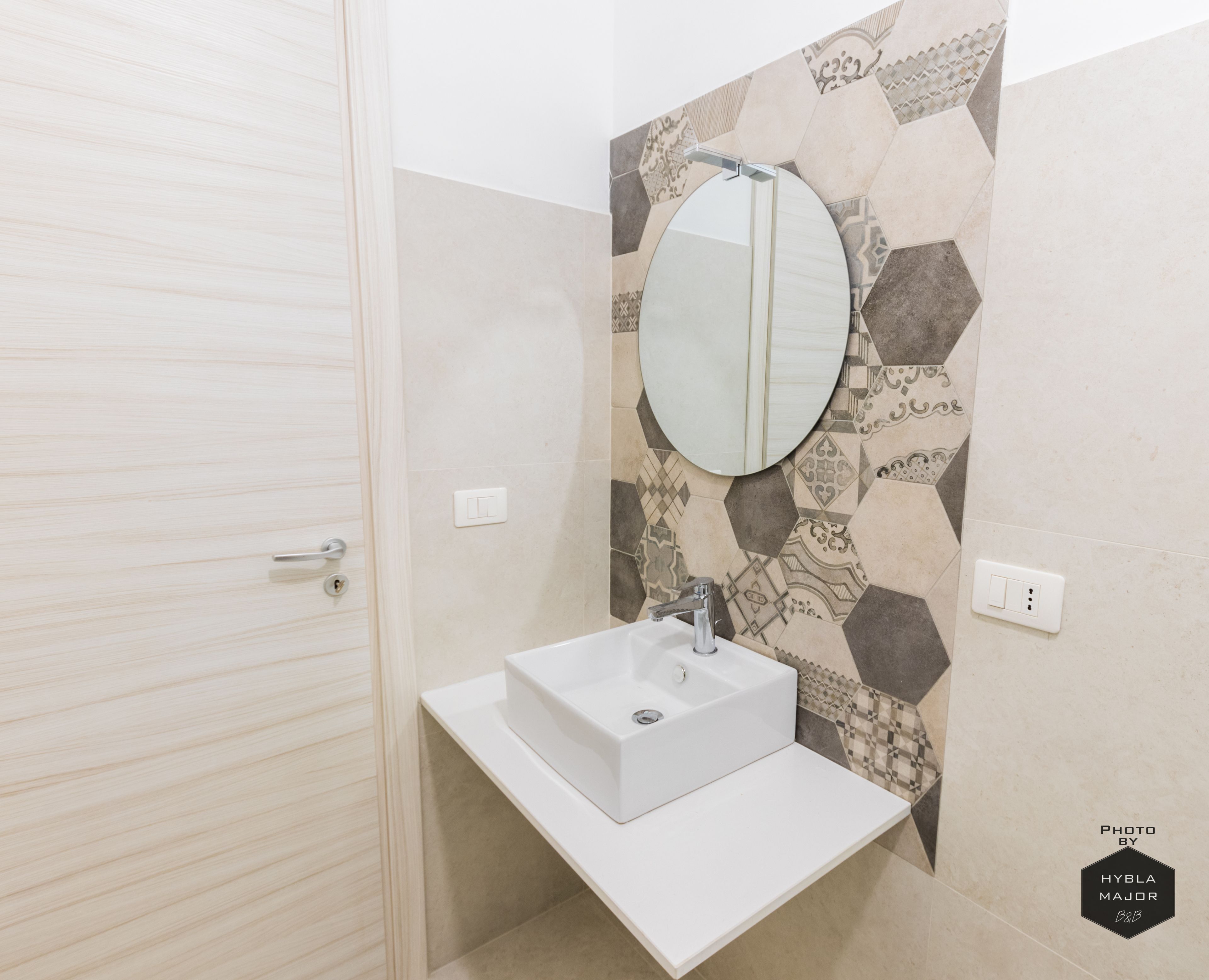 A bathroom with a white sink, a round mirror, and a patterned wall.