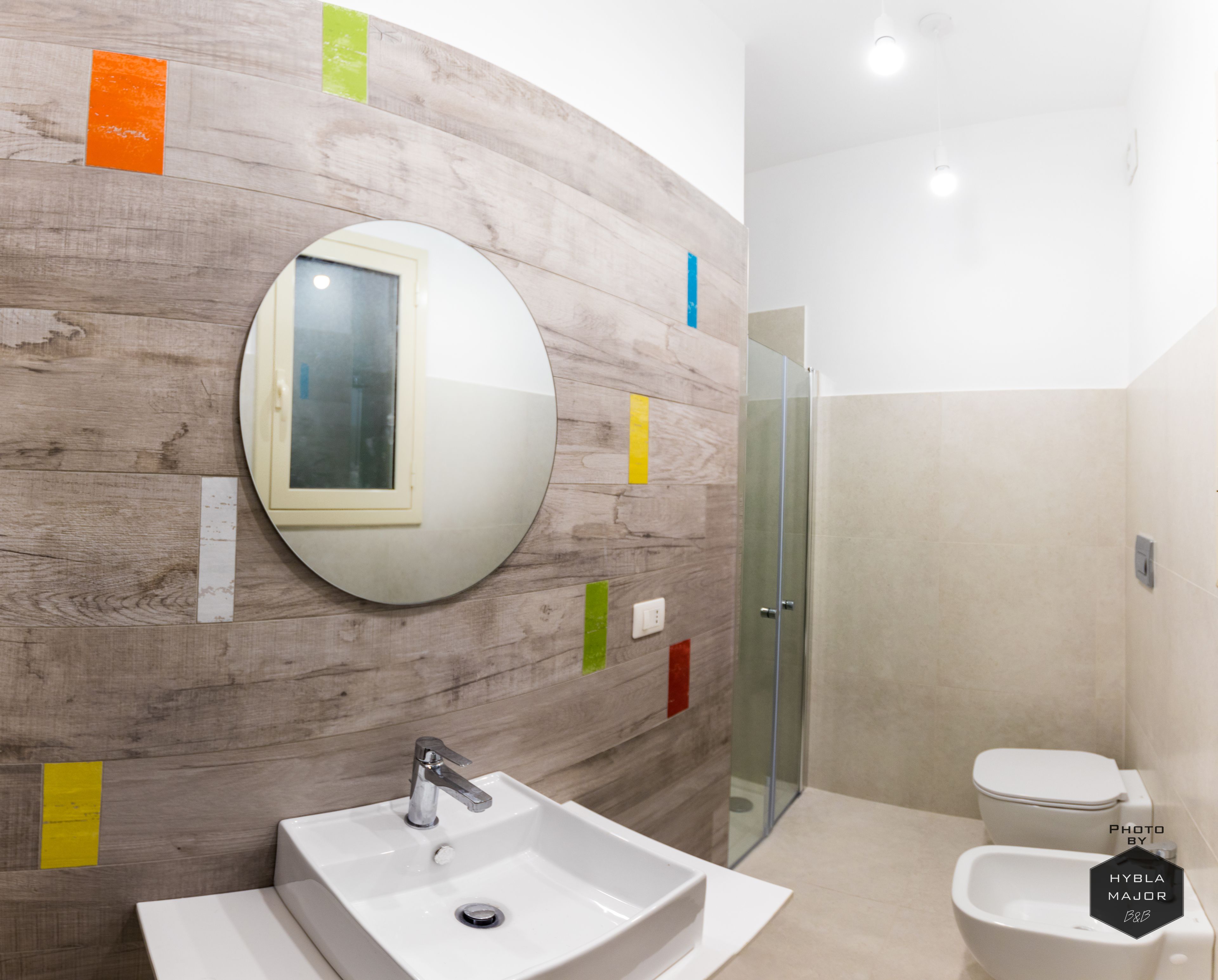 A modern bathroom with a round mirror, a sink, a toilet, and a glass shower enclosure.