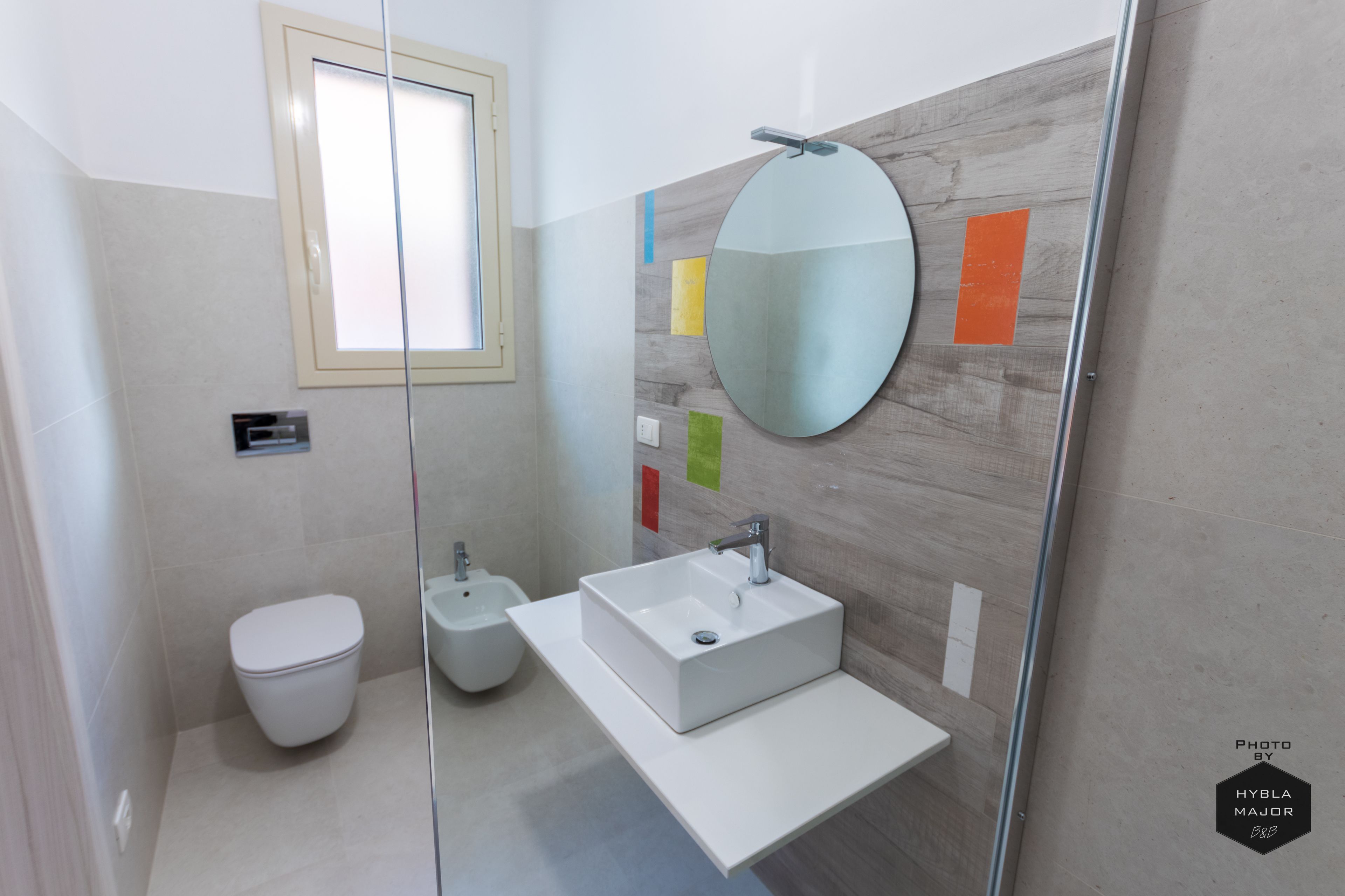 Een moderne badkamer met toilet, bidet en een grote spiegel boven een rechthoekig wastafel.