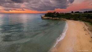 Paisaje costero con playa arenosa, mar tranquilo y un promontorio rocoso con vegetación.