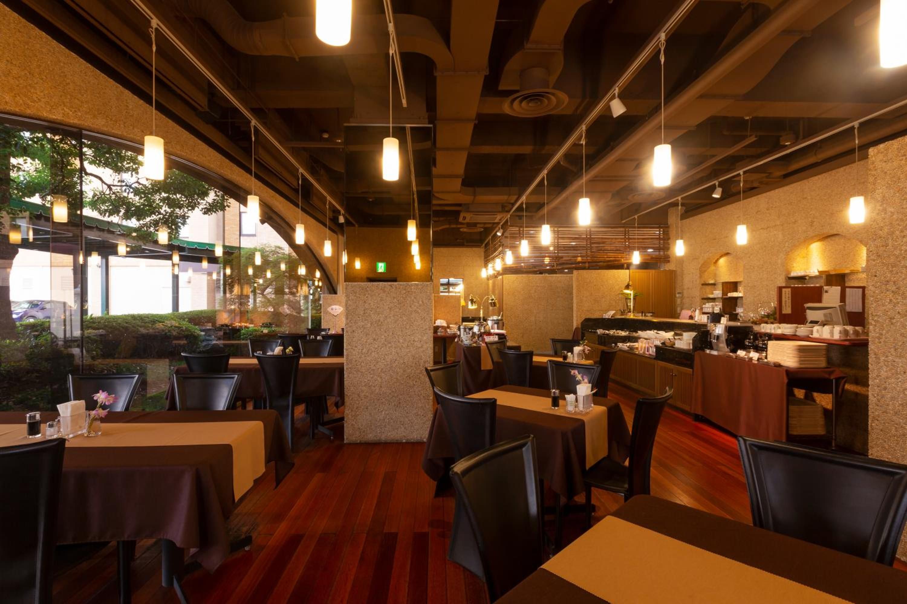 A restaurant with multiple tables and chairs, a kitchen area, and a view of the outdoors through large windows.