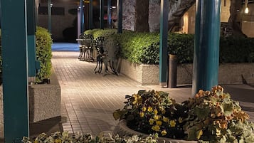 An outdoor area with a covered walkway, seating, and potted plants.