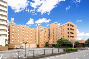 A multi-story hotel with a brick facade, a parking lot, and a clear blue sky. - Ohta Grand Hotel (Ota)