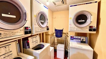 Un cuarto de lavandería con varias lavadoras y secadoras, incluyendo una cesta azul en un estante.