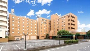 Un hotel de varios pisos con fachada plana, múltiples ventanas y un estacionamiento al frente.
