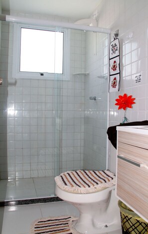 A bathroom with a shower, toilet, and a towel rack with a decorative item. - Palm Vilagge Acqua Flat (Ipojuca)