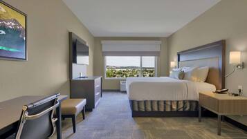 A hotel room with a bed, desk, chair, and a large window with a city view.