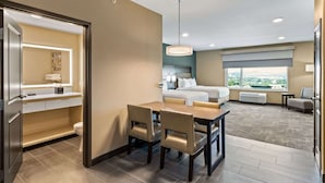 A hotel room with a dining area, a bed, a large window with a city view, and a bathroom with a toilet and sink. - Best Western Plus Fillmore Inn & Suites (Colorado Springs)