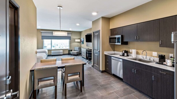 A modern hotel room with a dining area, kitchenette, and a large window offering a city view. - Best Western Plus Fillmore Inn & Suites (Colorado Springs)