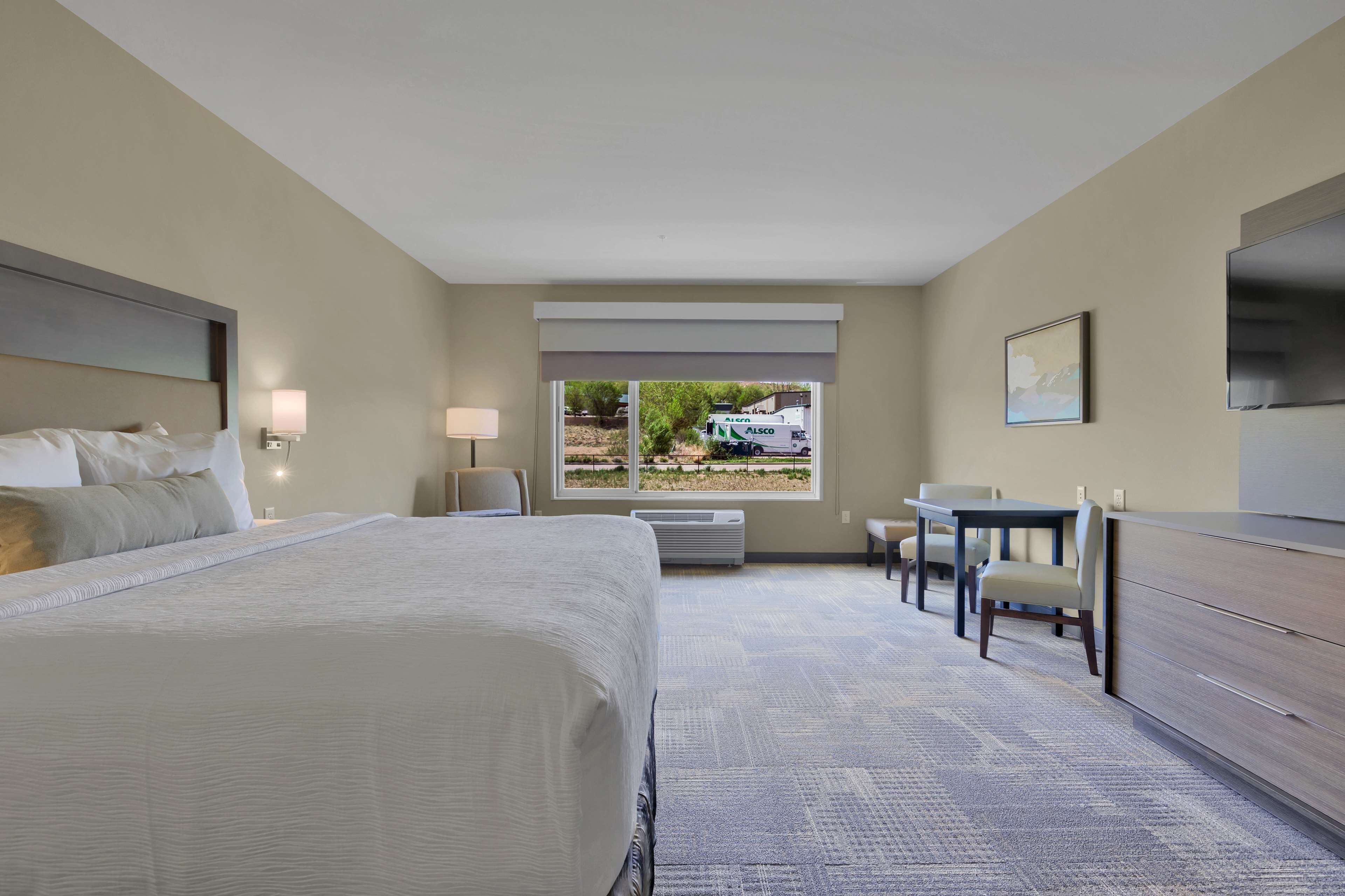 A hotel room with a large bed, a desk, a chair, a TV, and a window with a view of a truck outside.