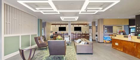 A modern hotel lobby with a reception desk, seating area, and a bar.