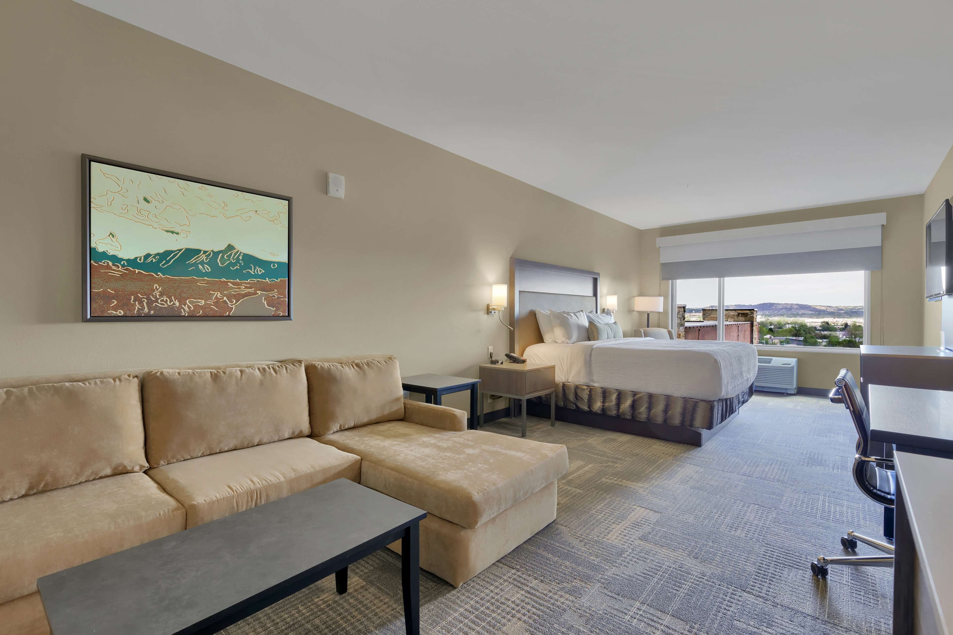 Habitación de hotel con sofá, cama, escritorio y un amplio ventanal con vistas al paisaje.