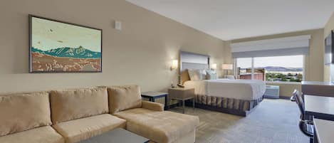 Habitación de hotel con sofá, cama, escritorio y un amplio ventanal con vistas al paisaje.