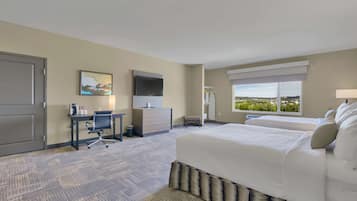 A hotel room with a large bed, a desk with a chair, a television, and a window with a view of greenery.