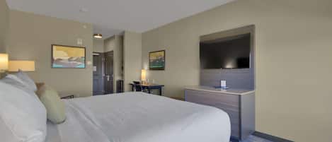 A hotel room with a large bed, a desk, a flat-screen TV mounted on the wall, and two paintings on the walls.