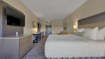 A hotel room with a large bed, a desk with a chair, a flat-screen TV mounted on the wall, and a small seating area with a couch.